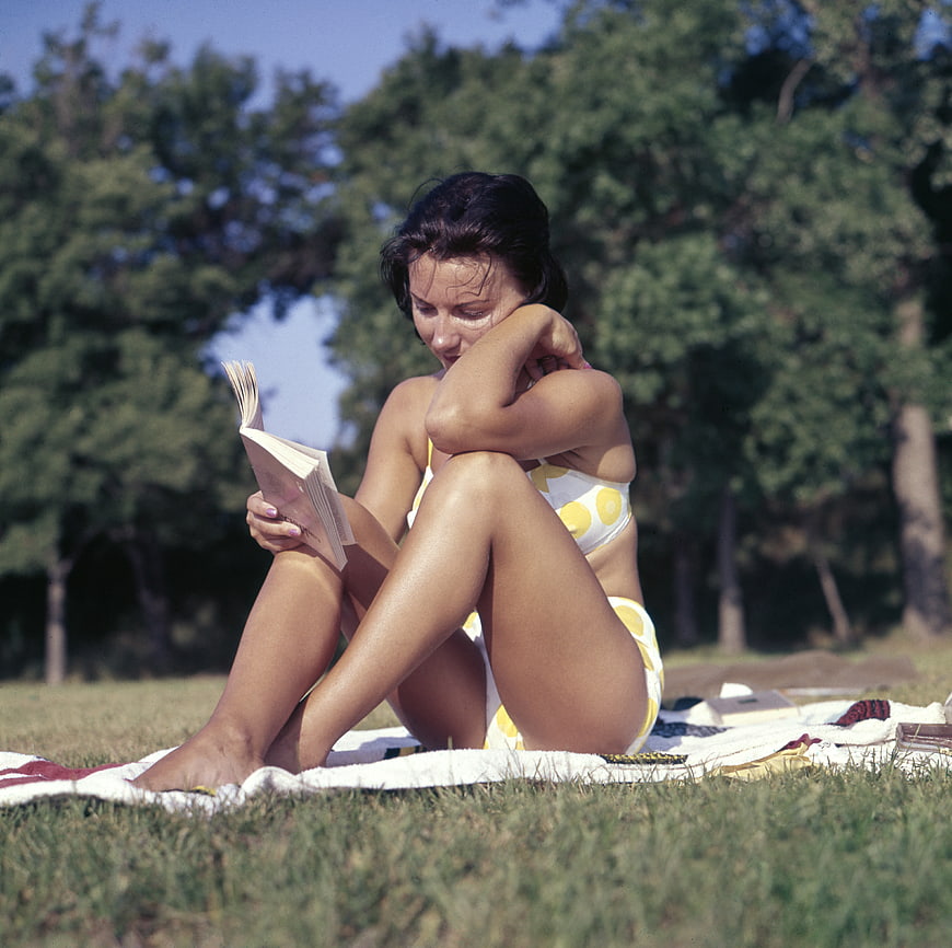 Vintage woman in yellow polka dot swimsuit reading on grass