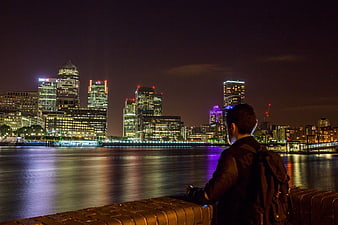 Man with Backpack Looking at London Canary Wharf Skyline at Night