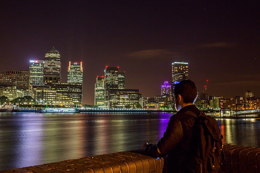 Man with Backpack Looking at London Canary Wharf Skyline at Night