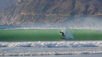 Surfer riding a large green wave near coastal cliffs