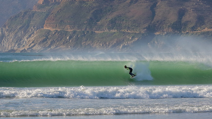 Surfer riding a large green wave near coastal cliffs