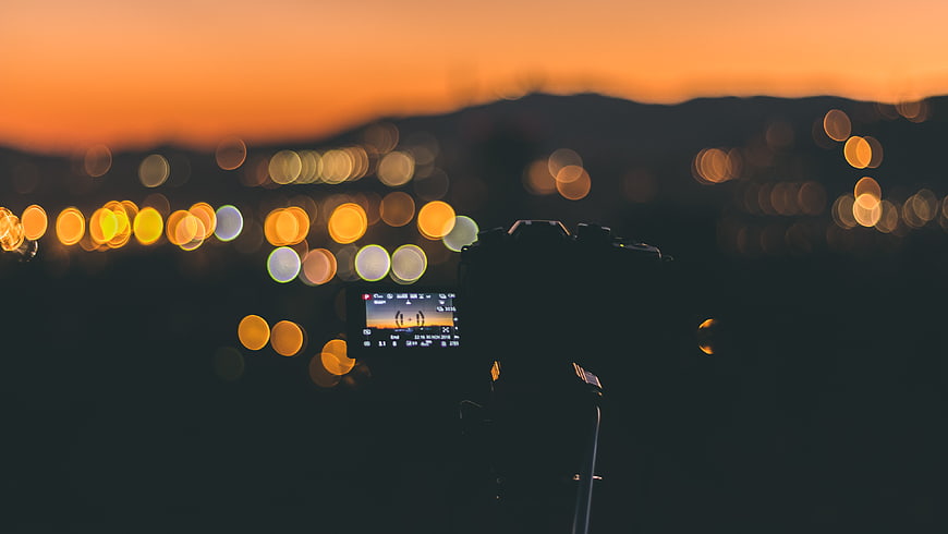 Camera on tripod capturing city bokeh at sunset