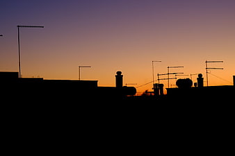 Silhouette of Rooftop Antennas Against Orange Sunset Sky