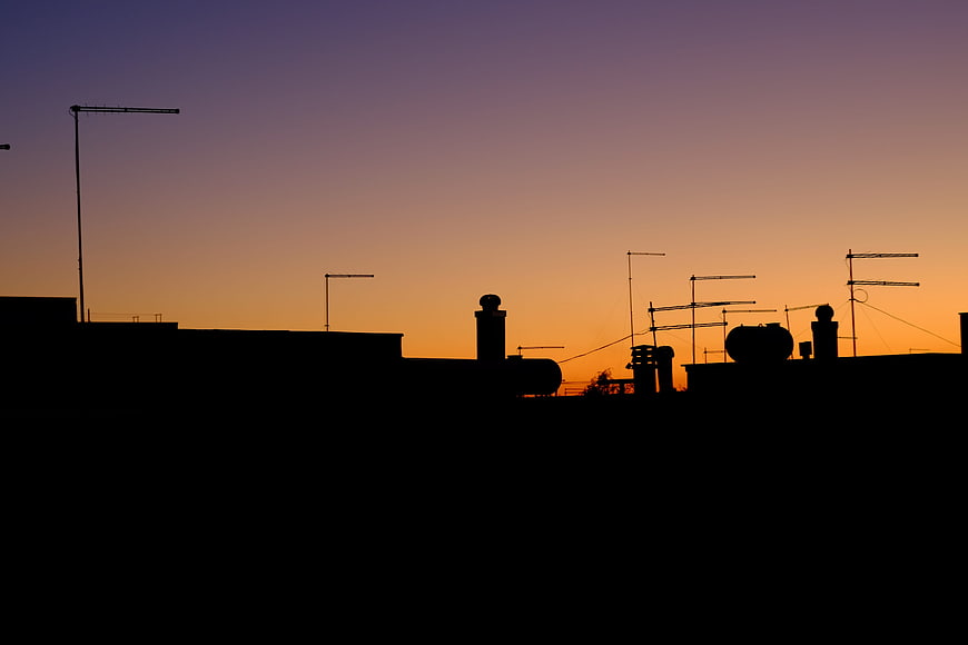 Silhouette of Rooftop Antennas Against Orange Sunset Sky