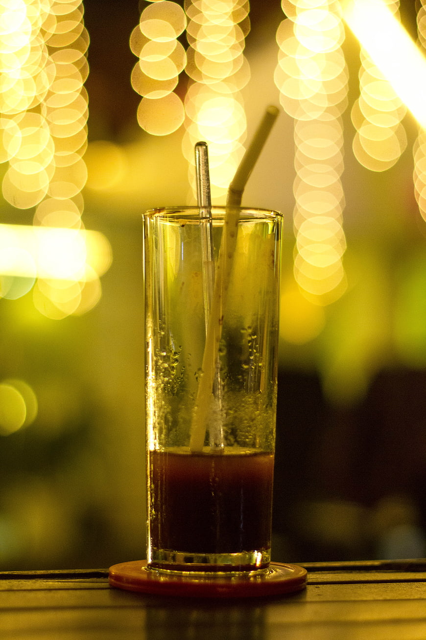 Half-empty cocktail glass with straws against bokeh lights