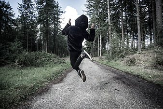 Person in black hoodie running away on forest road