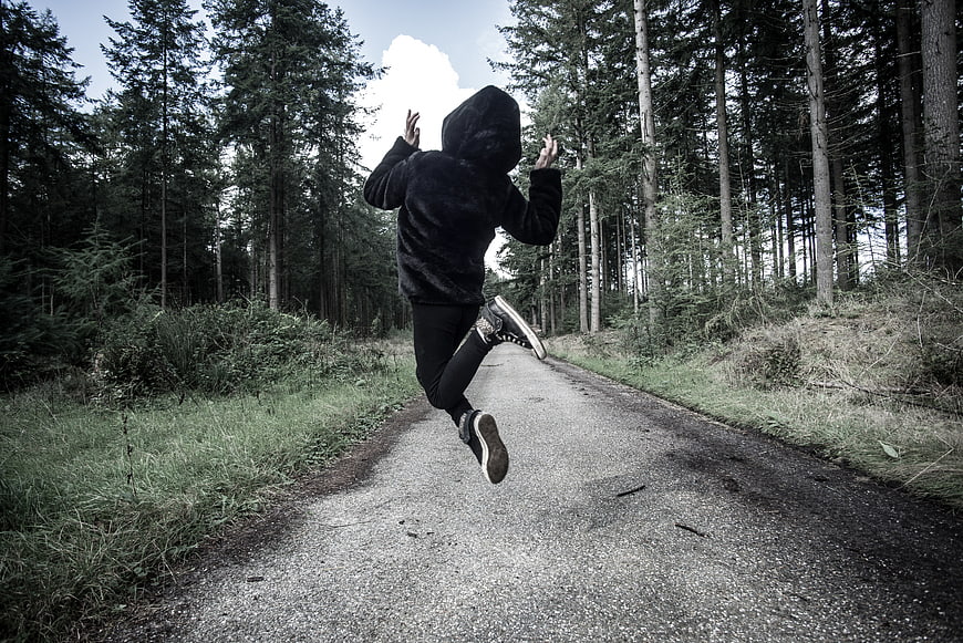 Person in black hoodie running away on forest road