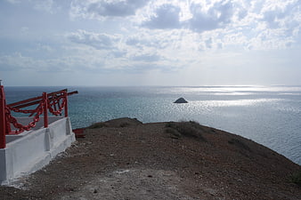Red railing on cliff overlooking ocean with rock formation