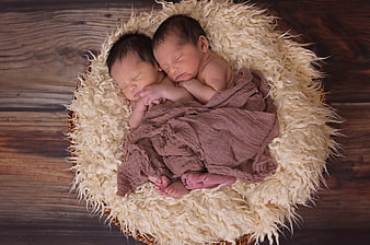 Newborn twin boys sleeping in a basket with faux fur