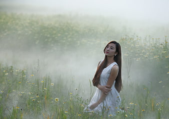 Woman in white dress standing in misty flower field