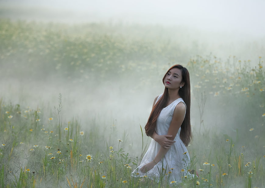 Woman in white dress standing in misty flower field