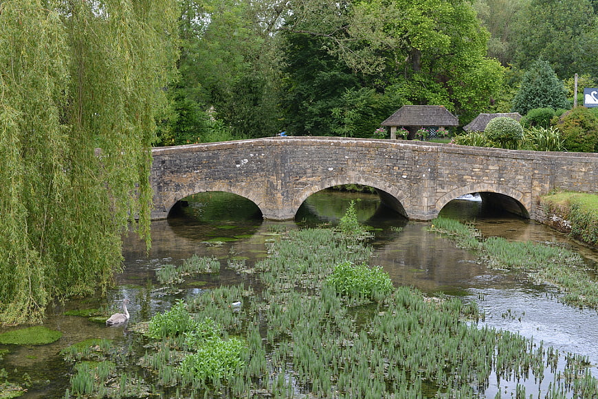 Stone arch bridge over river with swan and weeping willow