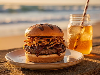 Gourmet BBQ Burger with Onion Strings on Beach at Sunset