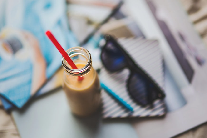 Flat lay of iced coffee bottle with sunglasses and notebook