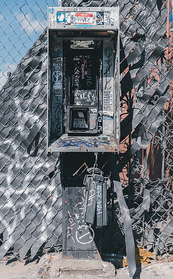 Abandoned Graffiti-Covered Payphone on Chain Link Fence