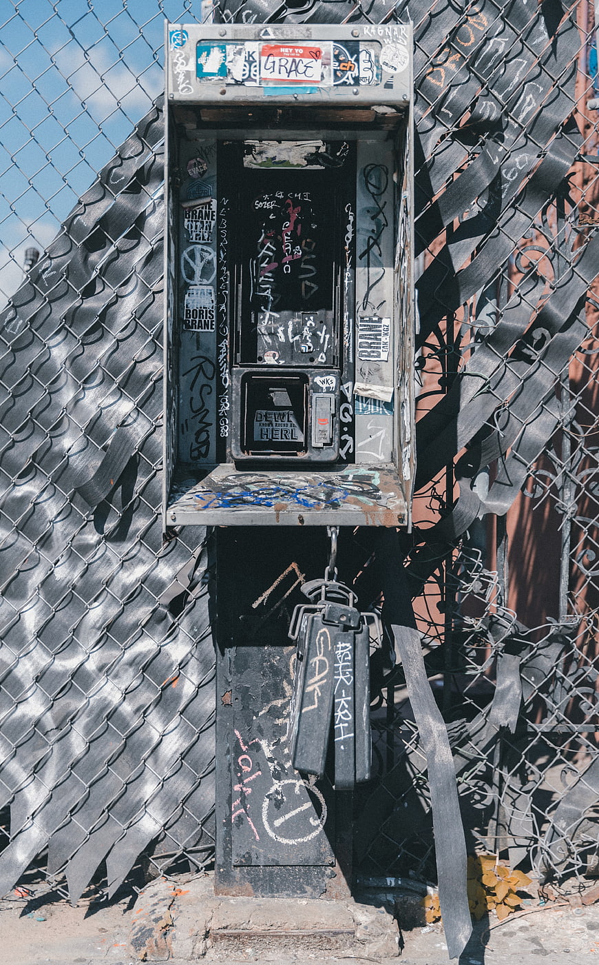 Abandoned Graffiti-Covered Payphone on Chain Link Fence
