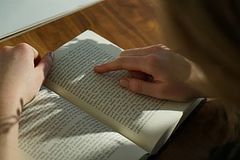 Close-up of hands reading a book on a wooden table