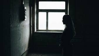 Silhouette of a woman standing in a dark room by a window