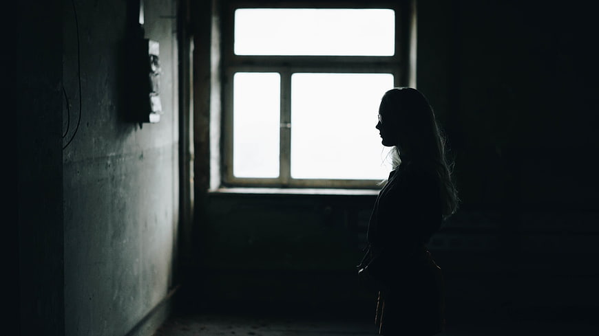 Silhouette of a woman standing in a dark room by a window
