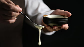 Chef pouring thick white cream from spoon into bowl