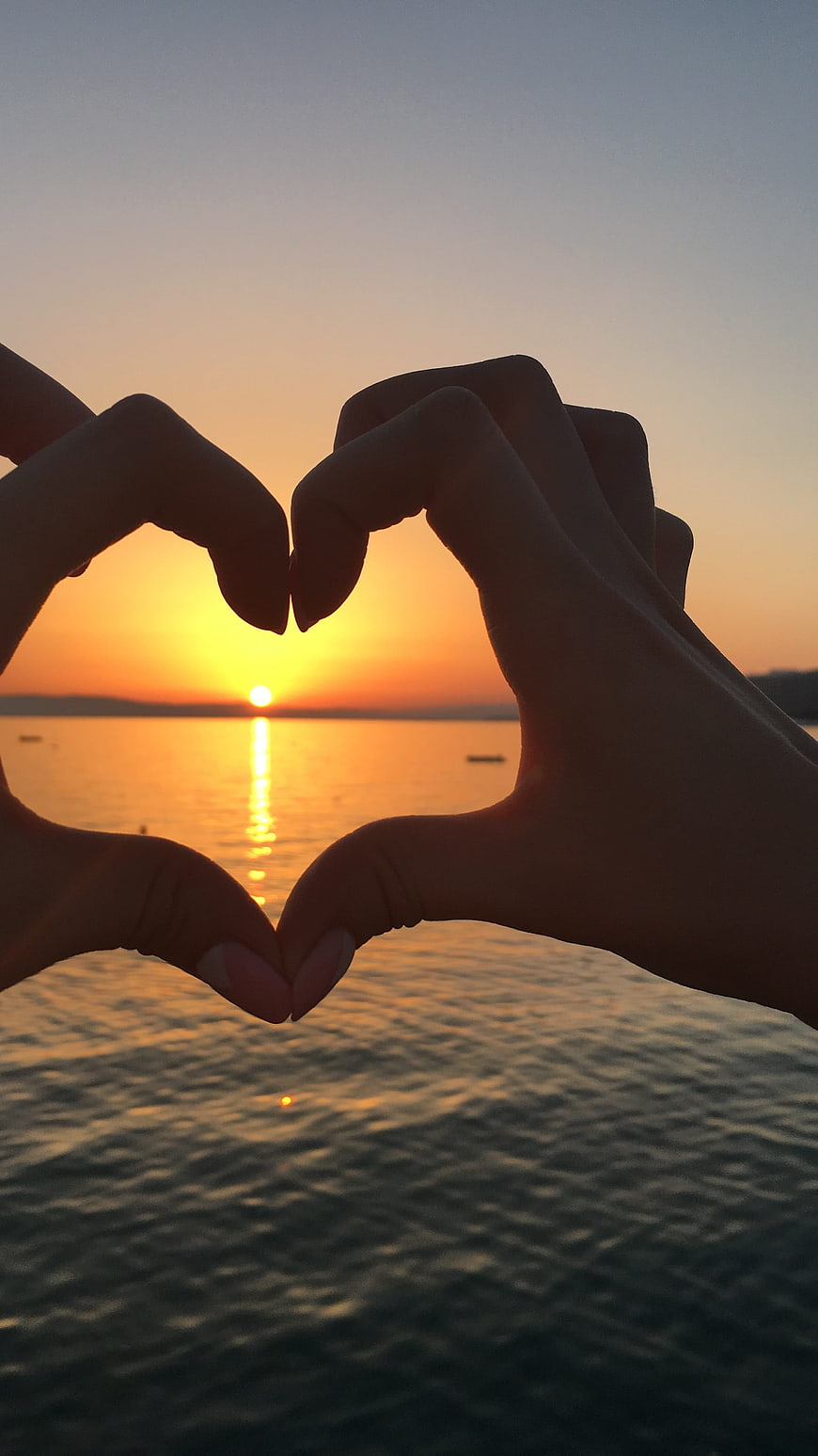 Hands forming heart shape framing sunset over ocean