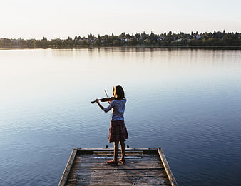 Girl playing violin on wooden dock by calm lake