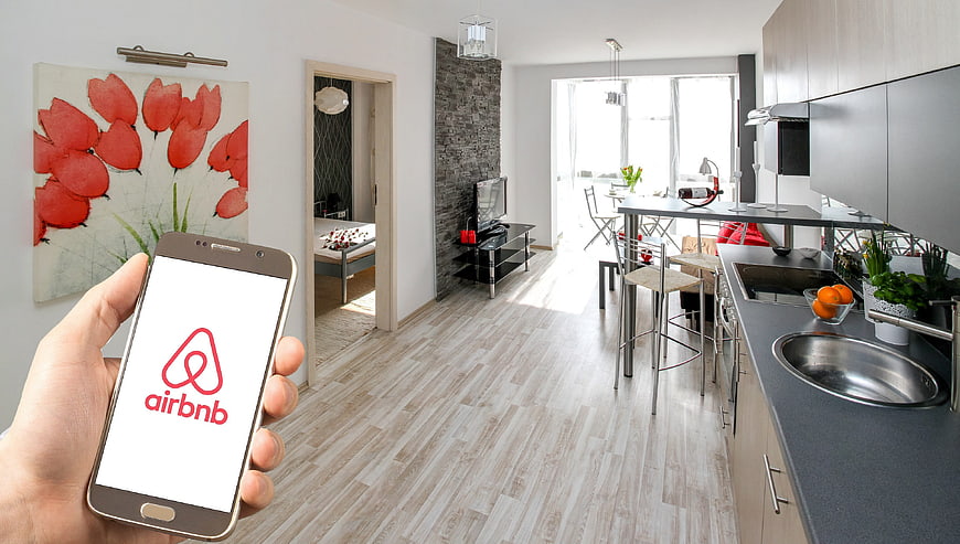 Hand holding smartphone with Airbnb app in modern apartment interior