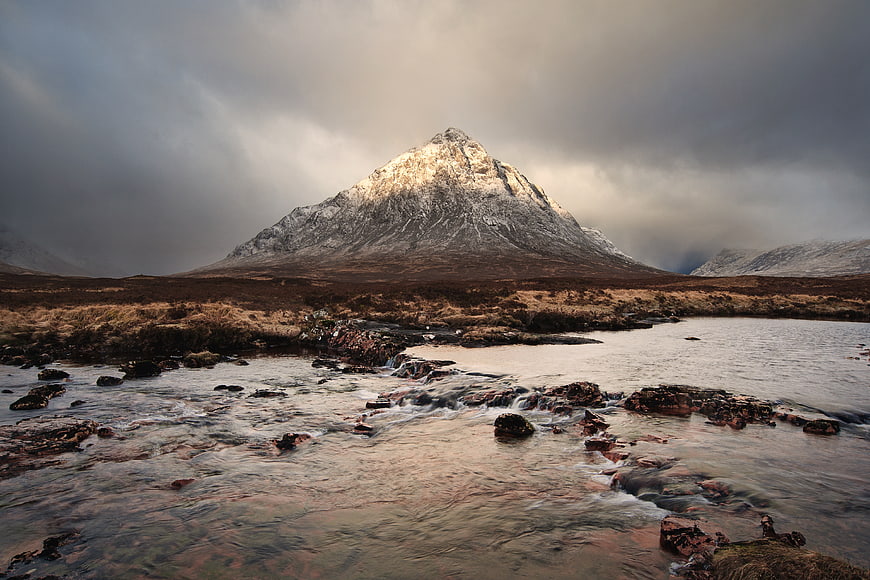 Dramatic Snow-Capped Mountain Peak with Flowing River Foreground