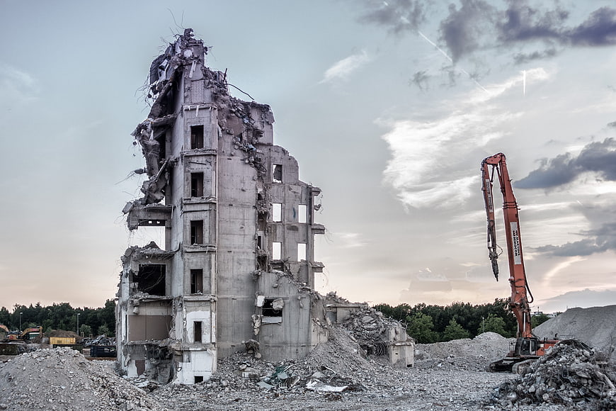 Demolition of concrete building with excavator at dusk