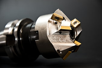 Industrial CNC milling cutter with gold carbide inserts on dark background