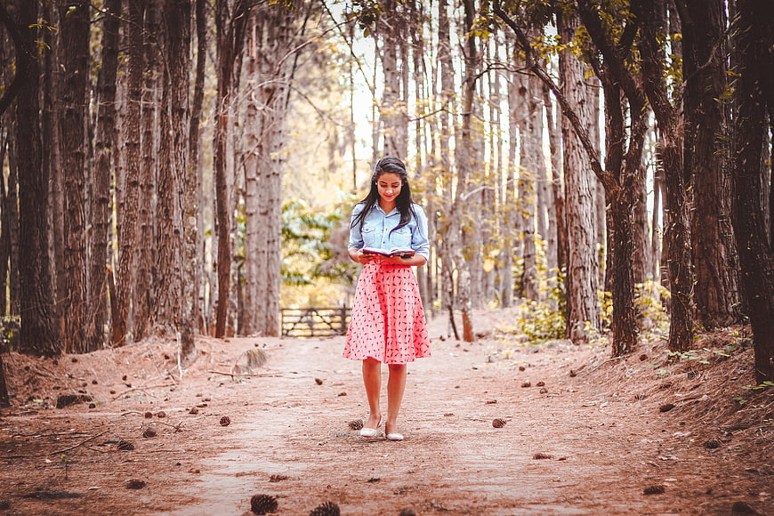Young woman reading a book while walking in a forest