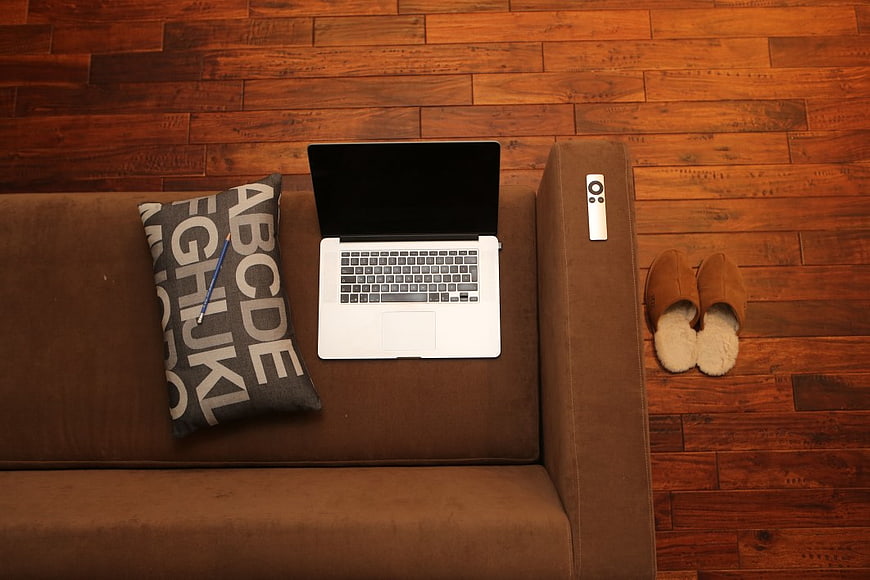 Top View of Laptop on Brown Couch with Slippers and Pillow