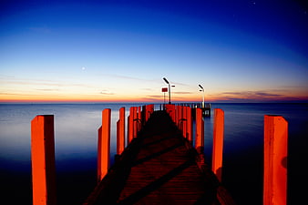 Wooden pier at sunset with orange posts and blue sky