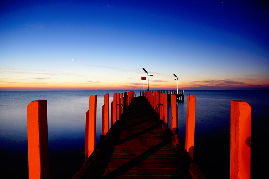 Wooden pier at sunset with orange posts and blue sky