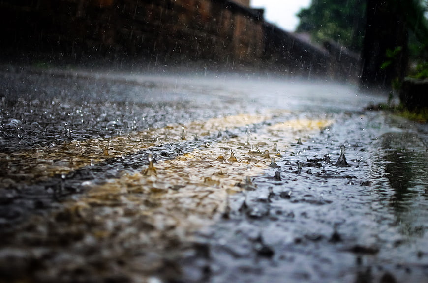 Raindrops splashing on wet asphalt road with yellow lines