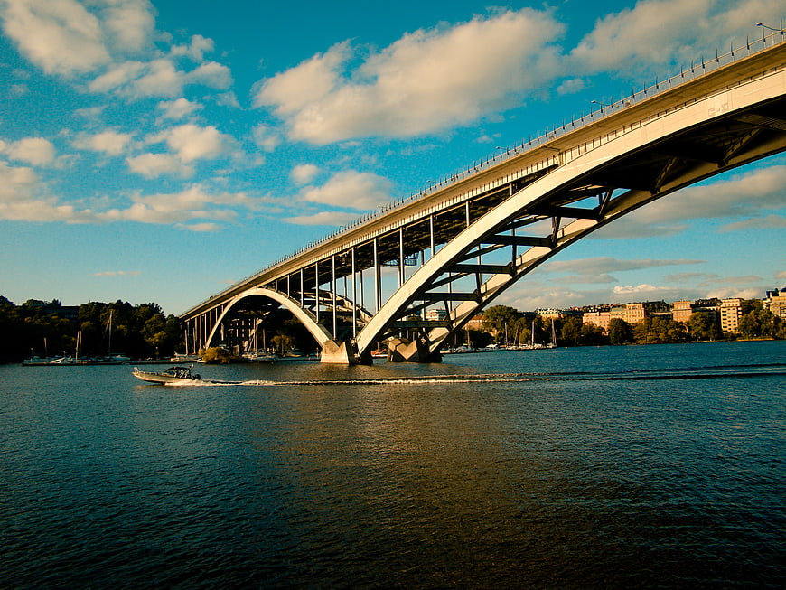 Modern Arch Bridge Over River with Speedboat and Blue Sky
