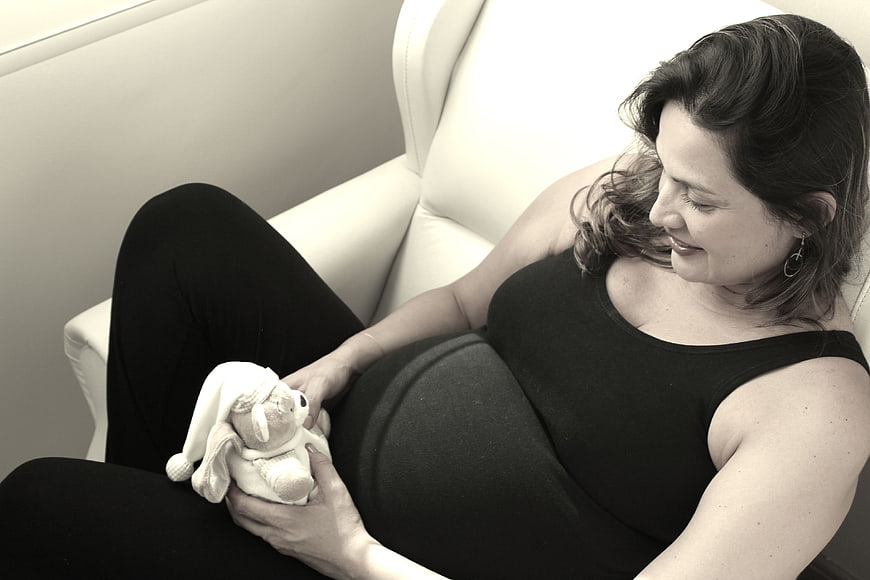 Pregnant woman holding stuffed bunny on white sofa