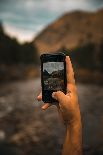 Hand holding smartphone taking photo of mountain river landscape