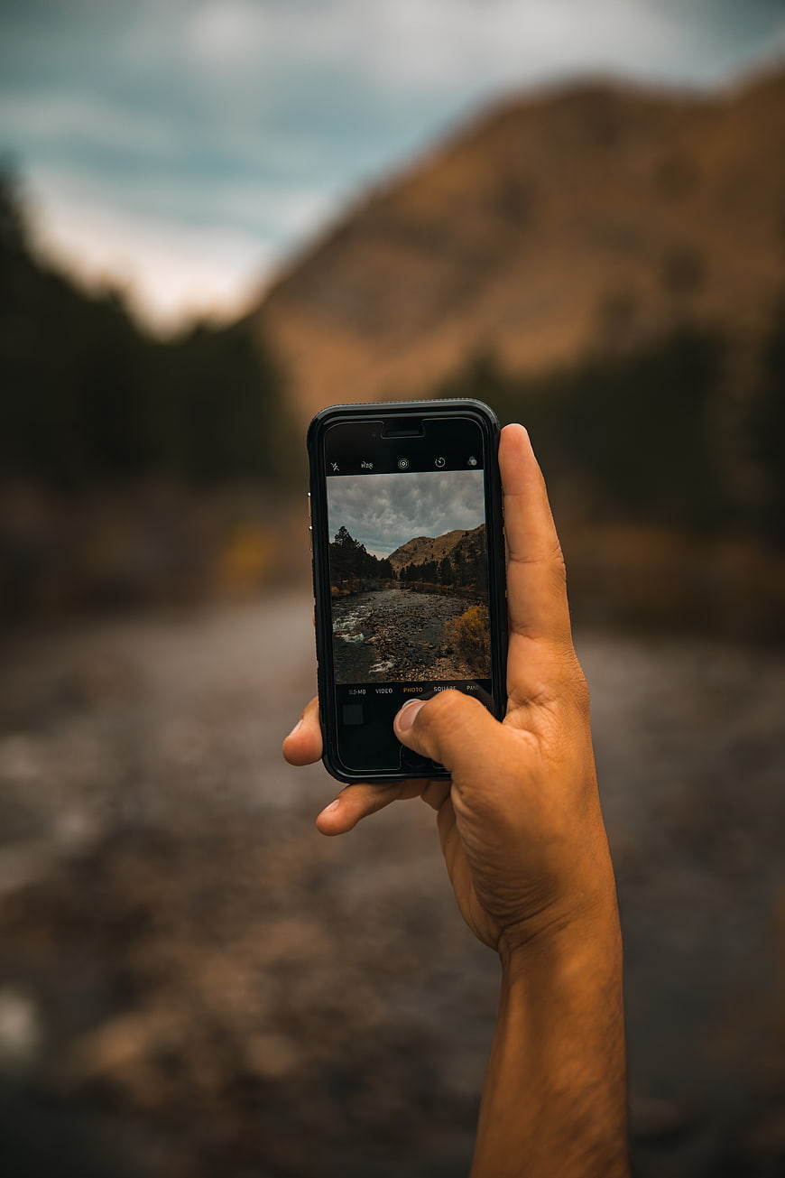 Hand holding smartphone taking photo of mountain river landscape