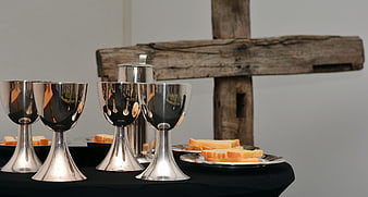 Silver chalices and communion bread arranged before a rustic wooden cross