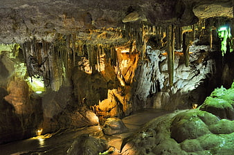 Illuminated limestone cave with stalactites and underground stream