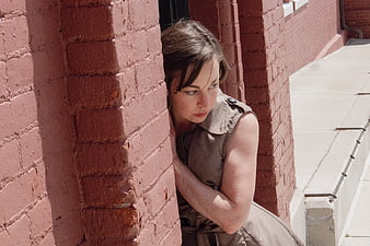 Woman leaning against red brick wall in sunlight