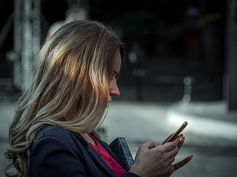 Woman with blonde hair texting on smartphone outdoors