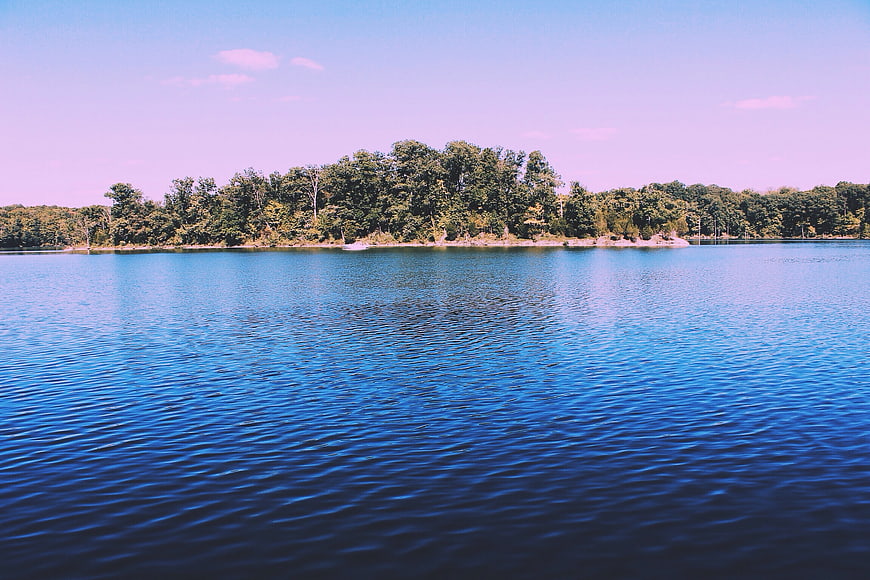 Serene blue lake with tree-lined island and purple sky