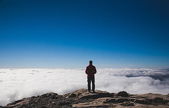 Man standing on mountain peak above sea of clouds