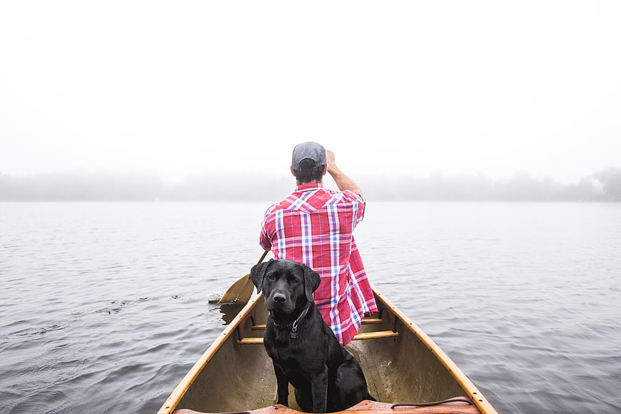 Man and Black Dog in Canoe on Foggy Lake
