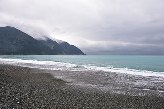 Misty turquoise ocean waves on a pebble beach with mountains