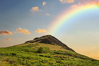 Vibrant rainbow arching over a green mountain peak at sunset