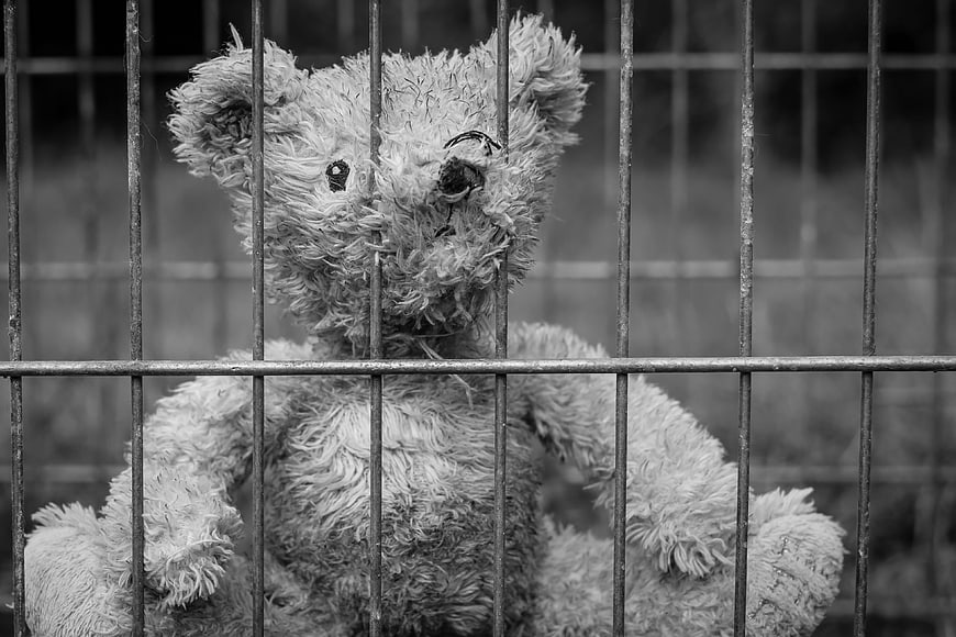 Lonely worn teddy bear behind metal cage bars