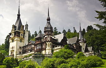 Peleș Castle in Romania with lush green forest and dramatic cloudy sky